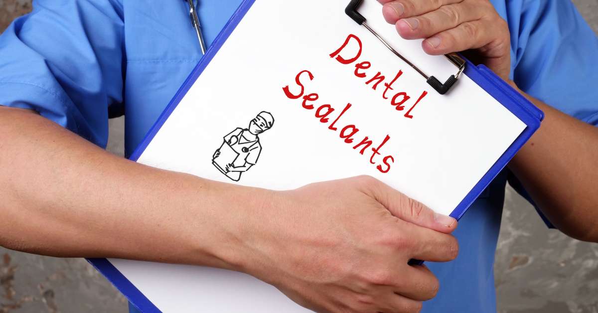 A medical worker in a blue shirt holds up a clipboard with a piece of paper that says "Dental Sealants" on it.