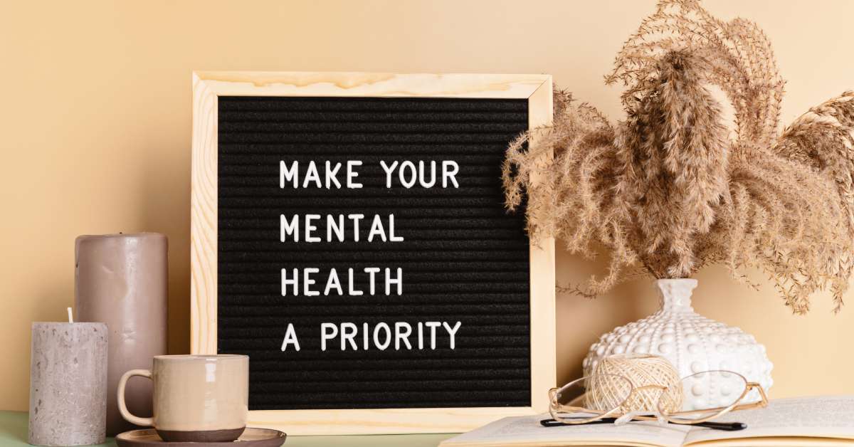 A letterboard leaning against a wall reads, "Make your Mental Health a Priority." It has a vase next to it.