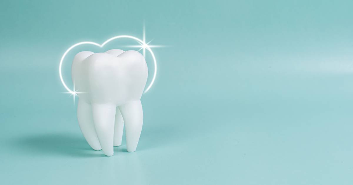 A white tooth is upright on a solid, light blue background. A white, shining halo hangs over the top of the tooth.