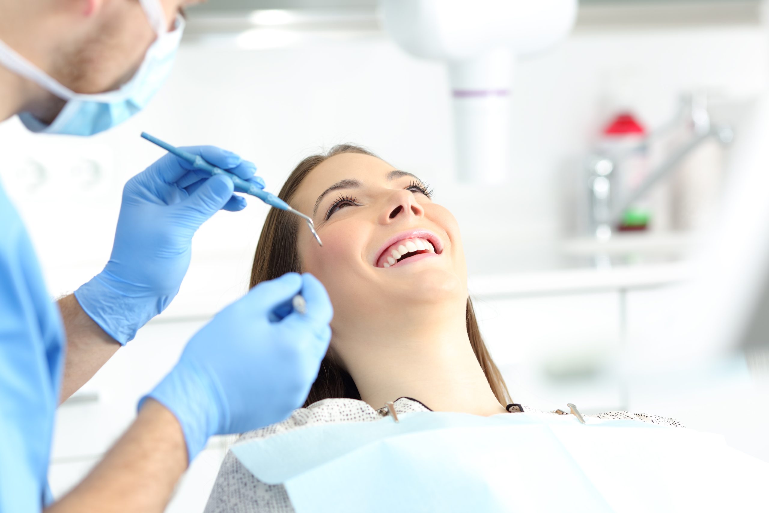 A dentist's patient smiles as she leans back in a chair. The dentist sits nearby, ready to clean her teeth.